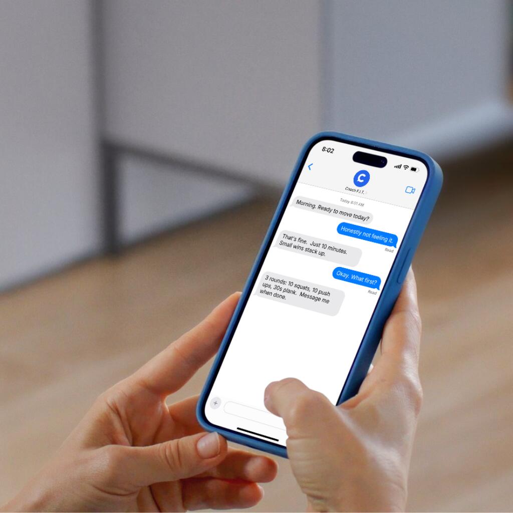 Hands holding a phone showing a text conversation with a coach, in a softly blurred home